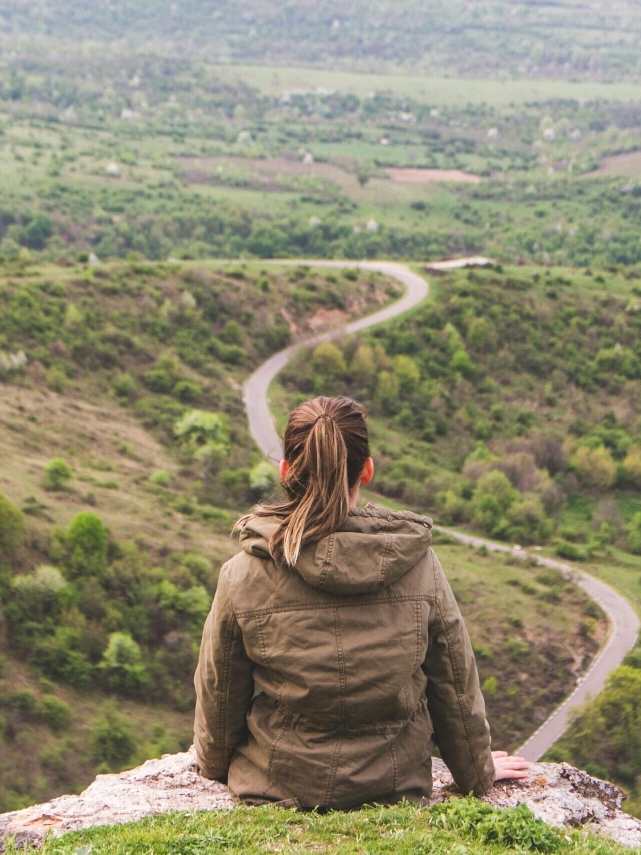 A person sitting on a hill looking at a winding road through green valleys