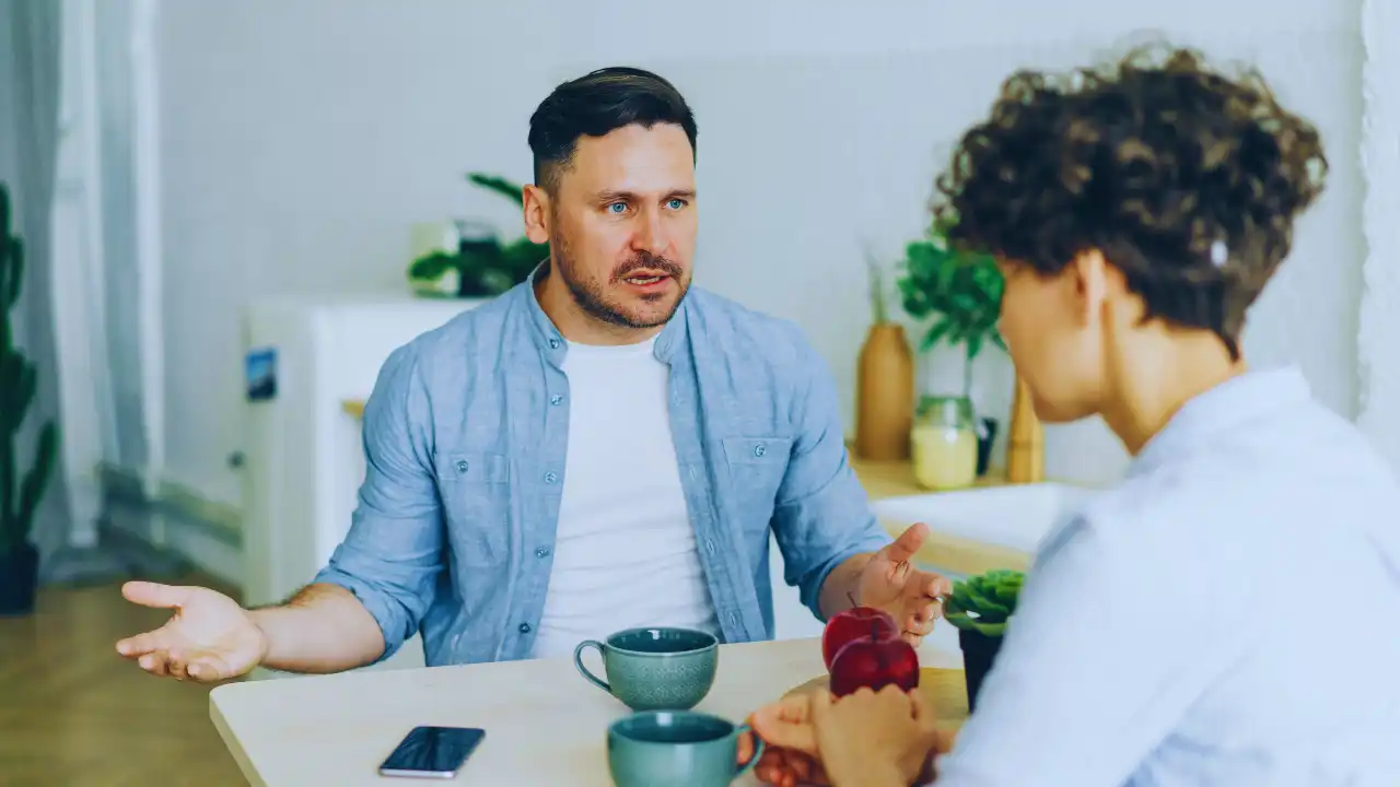 Two people having a conversation at a kitchen table.