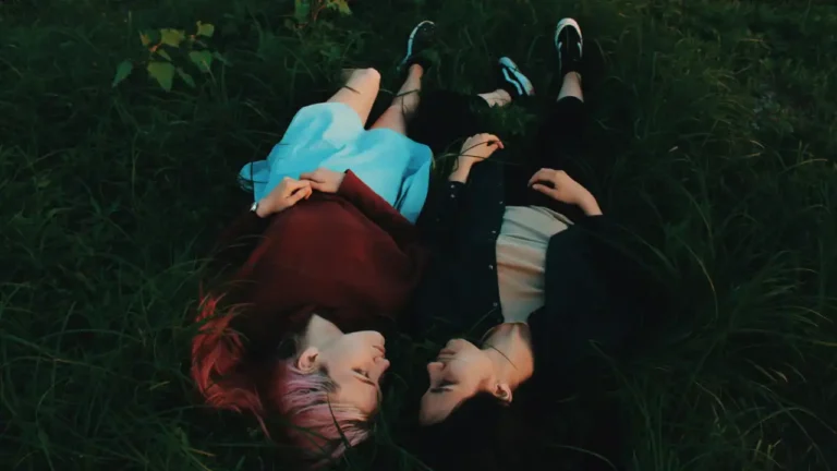Two people lying on grass, heads together, eyes closed