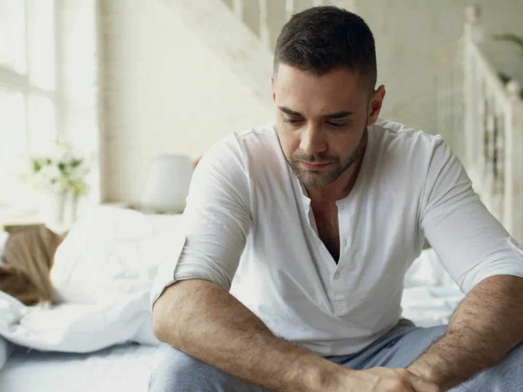 Man sitting on a bed looking down, thinking about resentment in his marriage