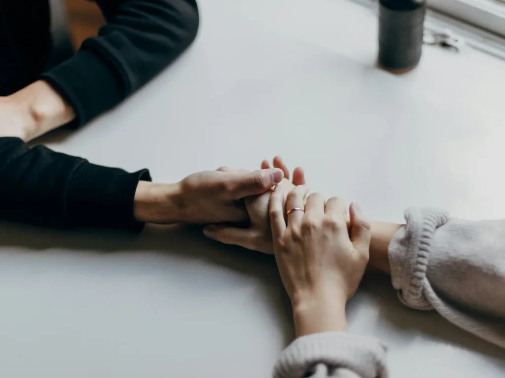 Two people holding hands on a table, working on their relationship in couples therapy