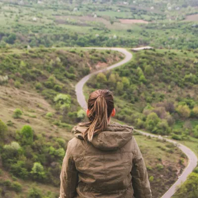 A person sitting on a hill looking at a winding road through green valleys